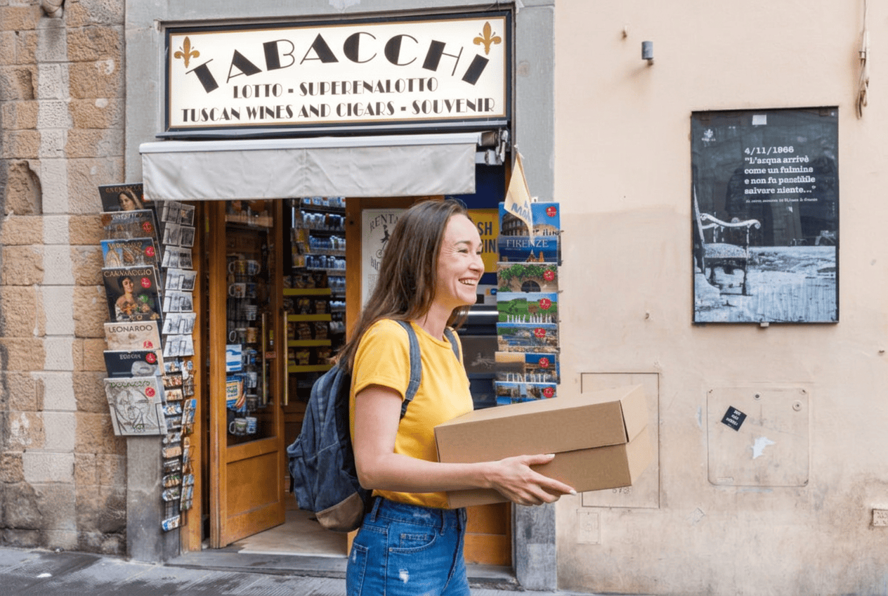 Ragazza caucasica sorridente esce da una tabaccheria con una scatola in mano